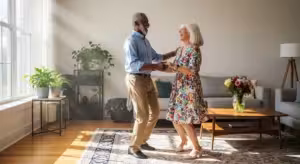 A happy senior couple dances energetically together in their sunlit living room, smiling and full of life.